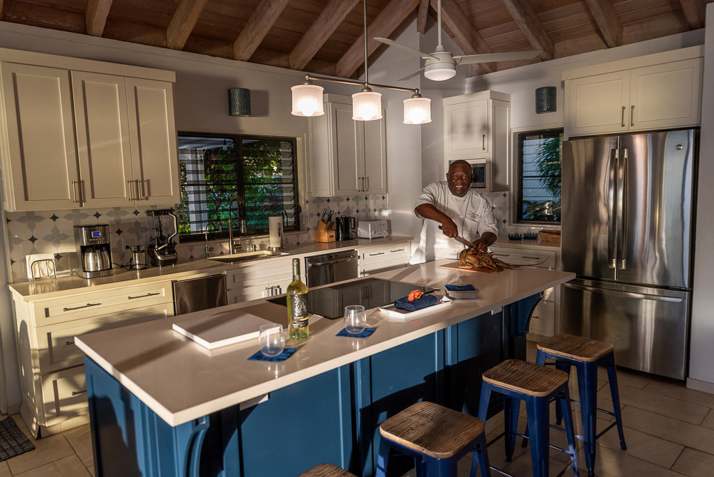 Chef preparing dinner in A Dream Come True Villa’s kitchen with white cabinets and counters and a large central island.