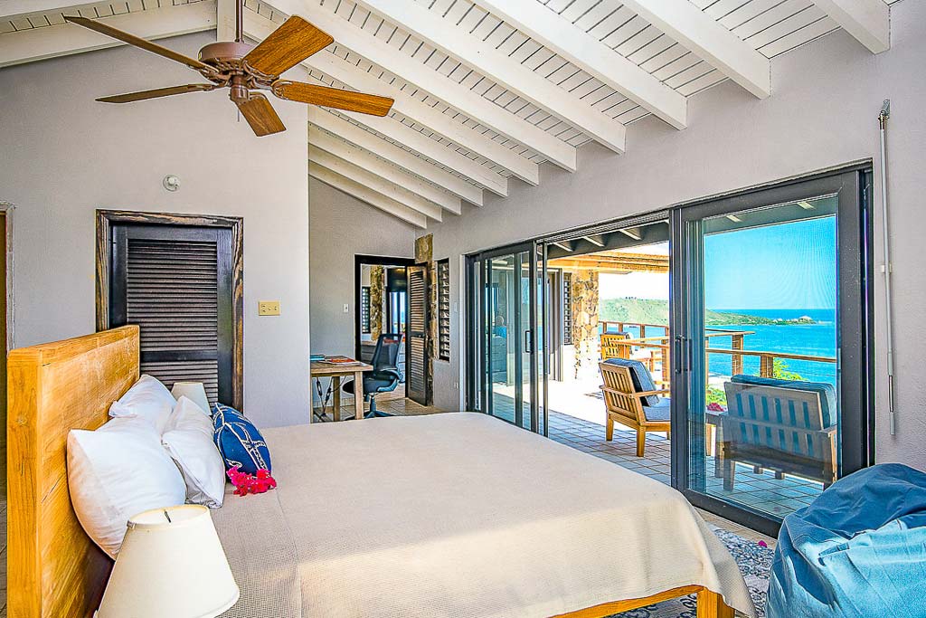 Master bedroom at Alize Villa with a king bed and table with a work desk and patio looking out on Leverick Bay in the background.