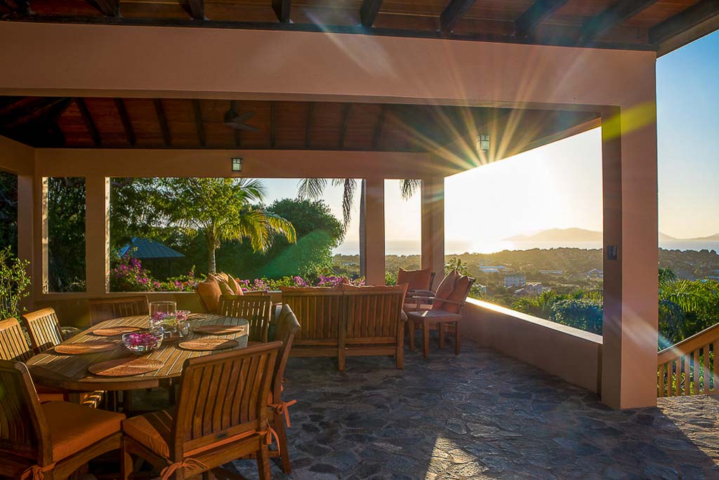 Covered porch at Amateras Villa with a dining area and separate living space and the island and a sunset in the distance.