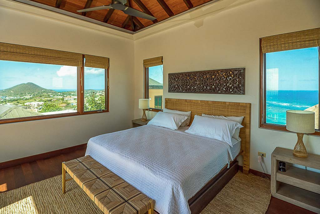 Amateras Villa’s master bedroom with a king bed, bed-side tables with lamps and windows looking out on the island and the sea.