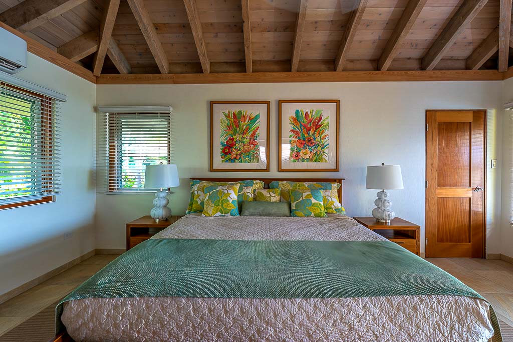 Beachcomber Villa’s master bedroom with a king bed and vaulted wood-beam ceiling and natural light coming through the windows.