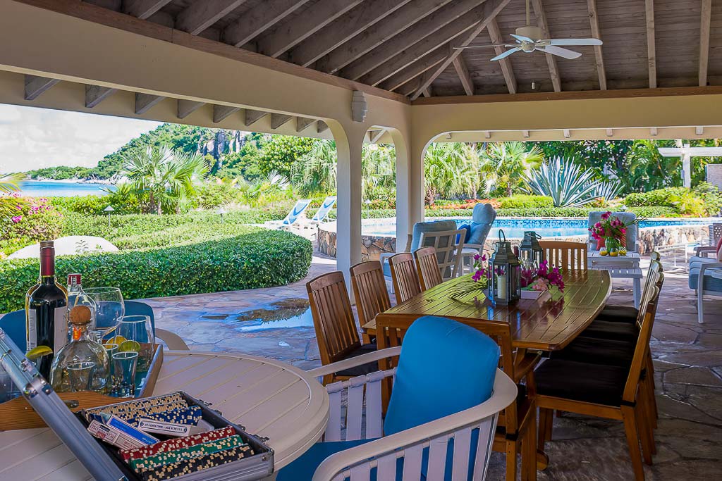 Outdoor dining area at Beachcomber Villa on a covered patio with a swimming pool and Mahoe Bay beach in the background.