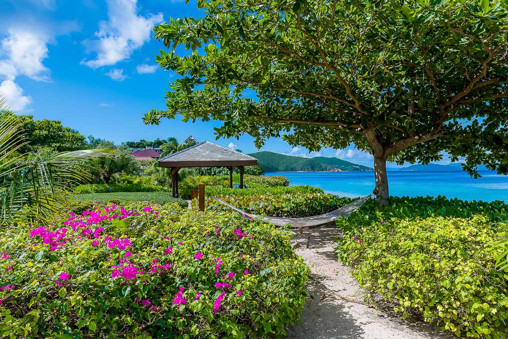 Beachcomber Villa’s tropical garden with a hammock tied to a tree next to the crystal blue waters of Mahoe Bay, Virgin Gorda.