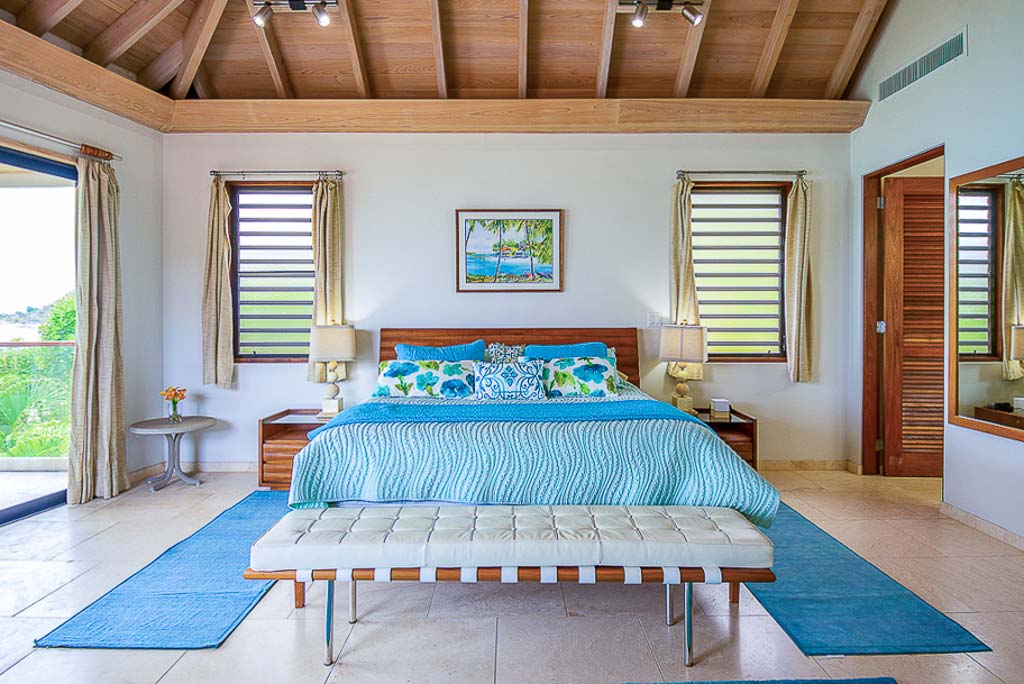 Master bedroom at Caribbean Wind Villa with a king bed, lofted wood-beam ceilings and a door leading to a pool patio.