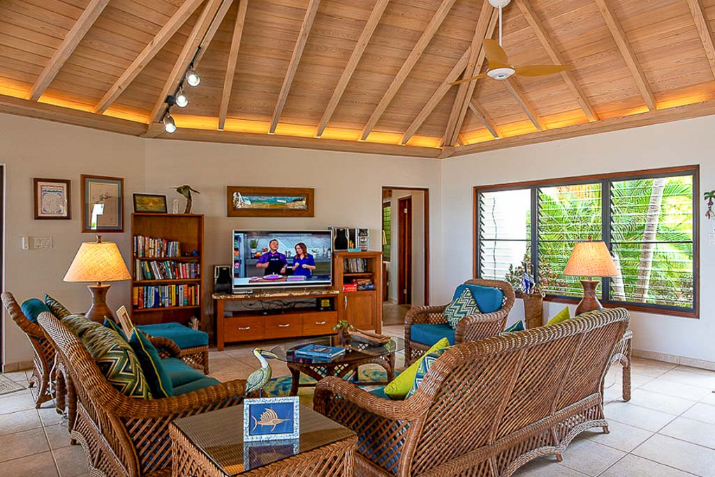 Caribbean Wind Villa’s great room with a conversation seating area with wicker furniture and a library and flat-screen TV.