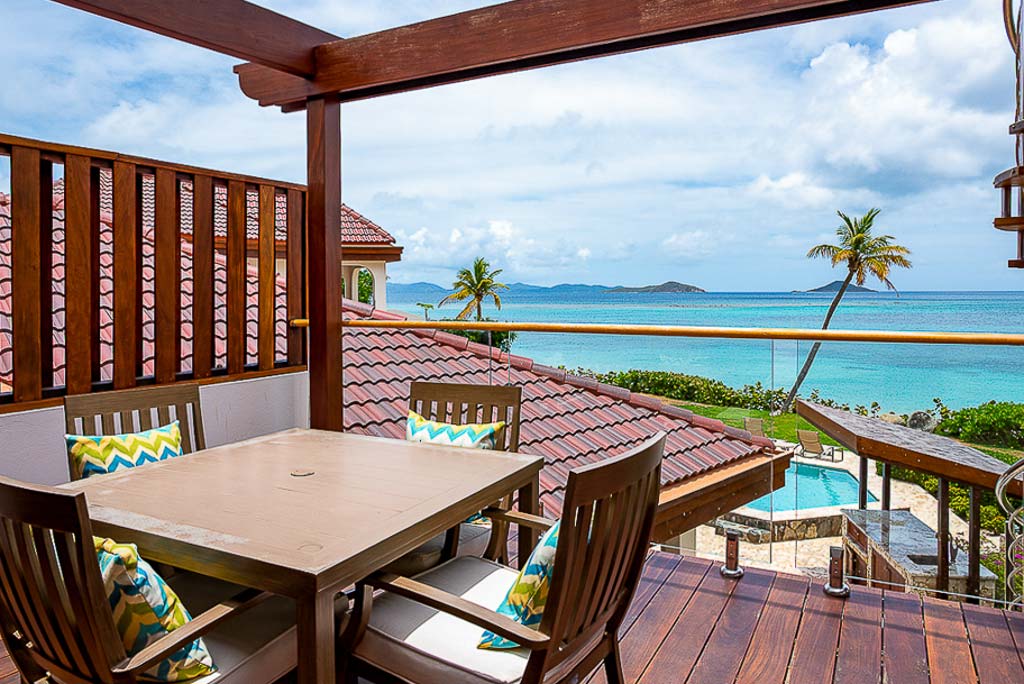 Roof-top patio with a table and chairs at Caribbean Wind Villa at Mahoe Beach with a pool and the sea in the background.
