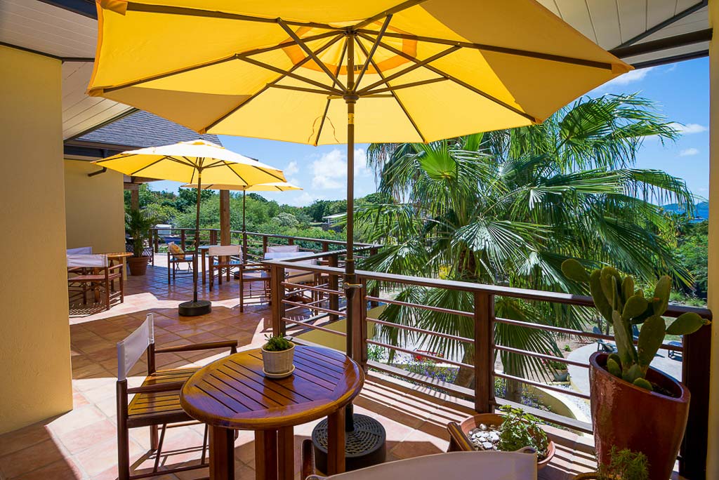 Wood tabletops with yellow umbrella stands along the elevated, wrap-around tile patio at Cornucopia Villa in Virgin Gorda.