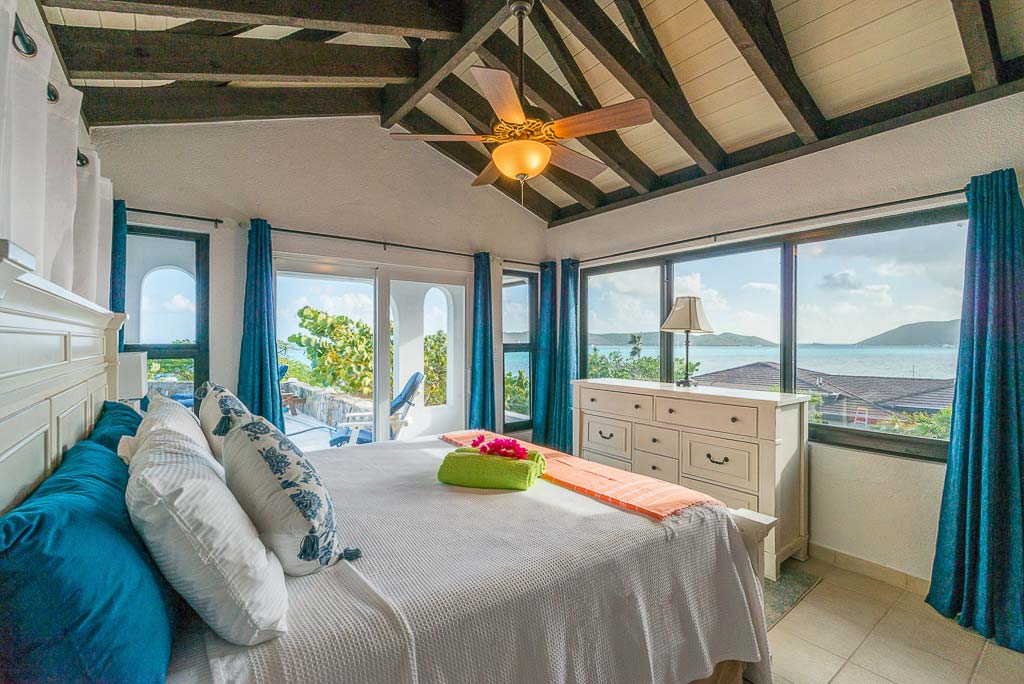 Guest bedroom at Euphoria villa with a king bed and wood-beam ceiling and glass doors leading to an elevated patio.