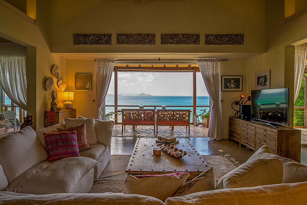 Living room at La Vida Villa with a comfortable wrap-around couch and coffee table and an open door looking out on Nail Bay.