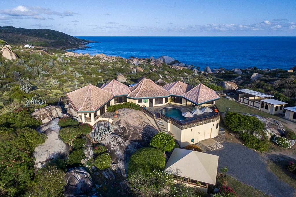 Mon Repos Villa with a natural stone exterior and tile roof on a hillside dotted with boulders with the sea in the background.