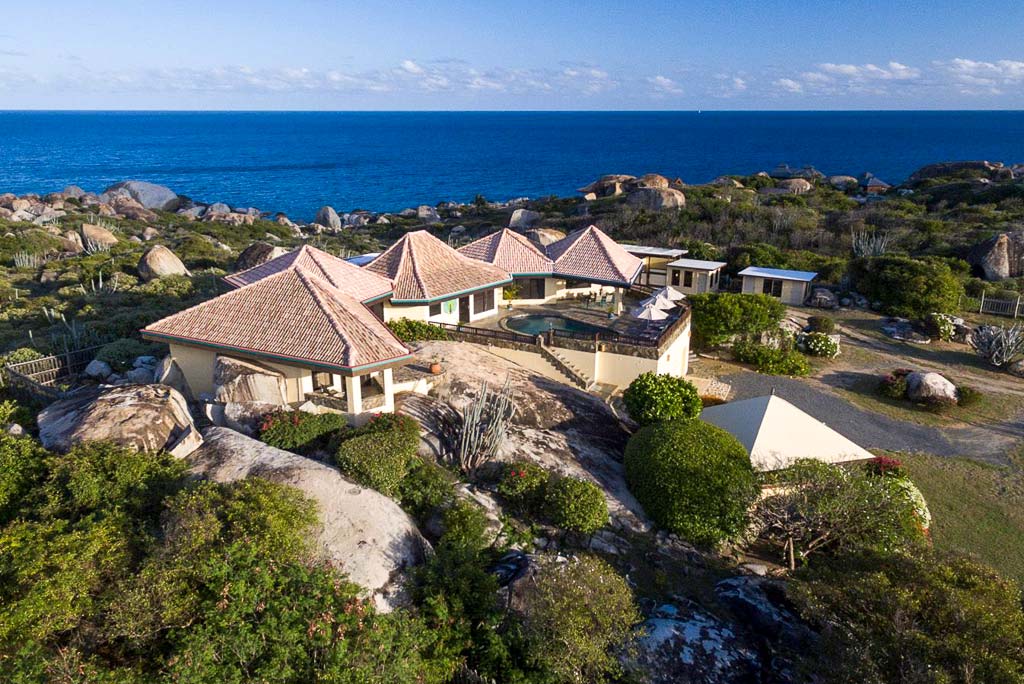 Mon Repos Villa with a natural stone exterior and tile roof and a pool patio with the blue Caribbean waters in the background.