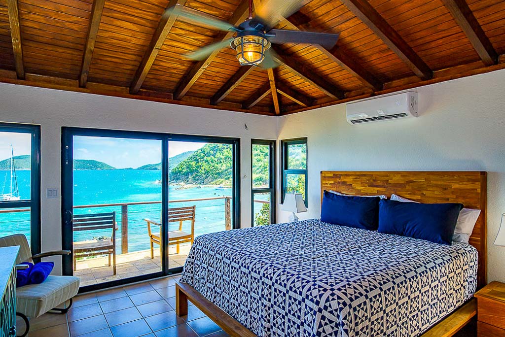 Master bedroom at Rainbow’s End Villa with a private patio overlooking the beach, blue water and sailboats on Leverick Bay.