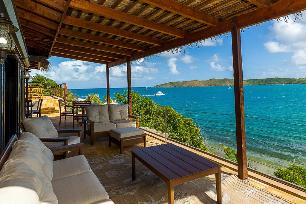 Covered patio with comfortable outdoor furniture at Rainbow’s End villa with a background of the waters of Leverick Bay.
