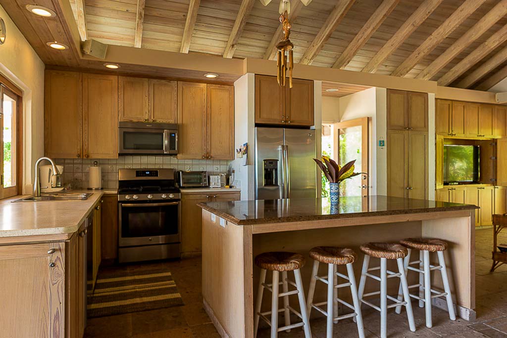 Open kitchen in Sea Fans Villa’s main room with light wood cabinets and granite counter tops and a large island with stools.