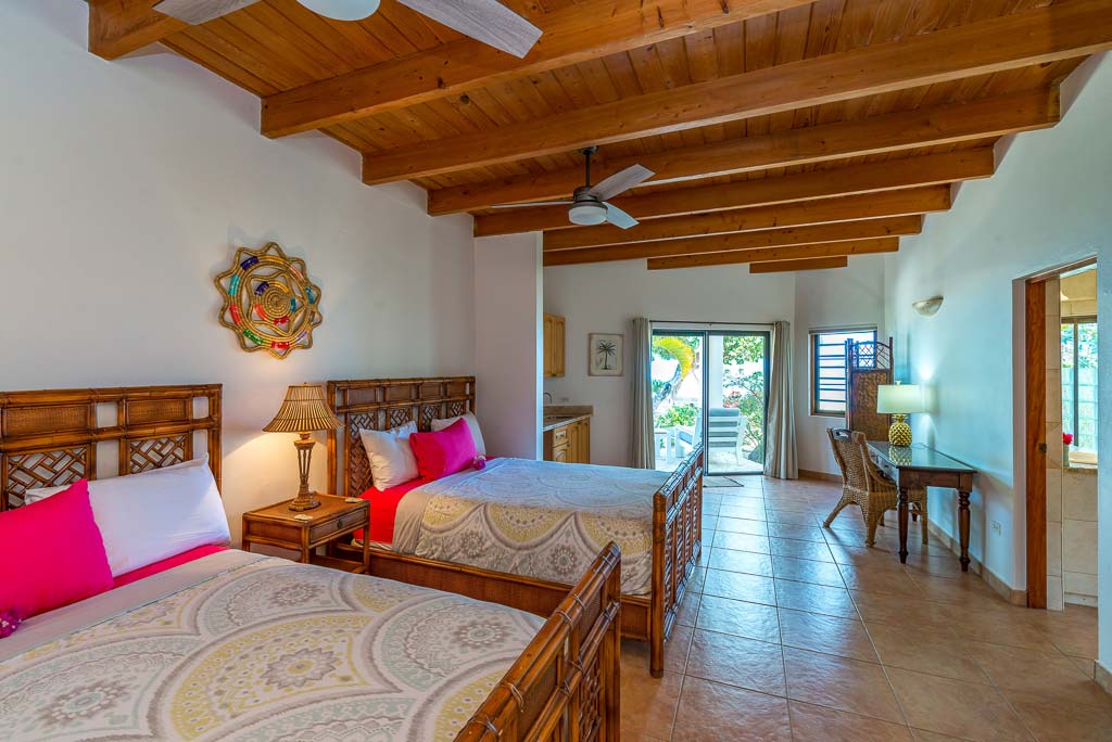Sea Palms Villa guest room with two double beds, tile floors, wood ceiling with fans and glass door leading to a patio area.