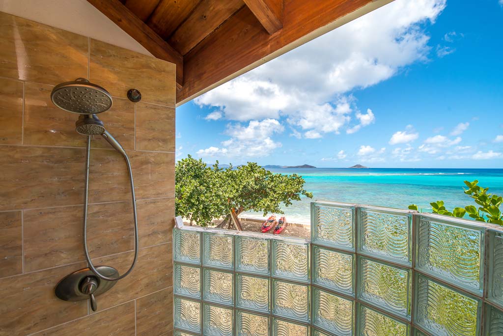 Indoor/outdoor shower at Sea Palms Villa with Mango Bay beach and calm blue water and sunny skies in the background.