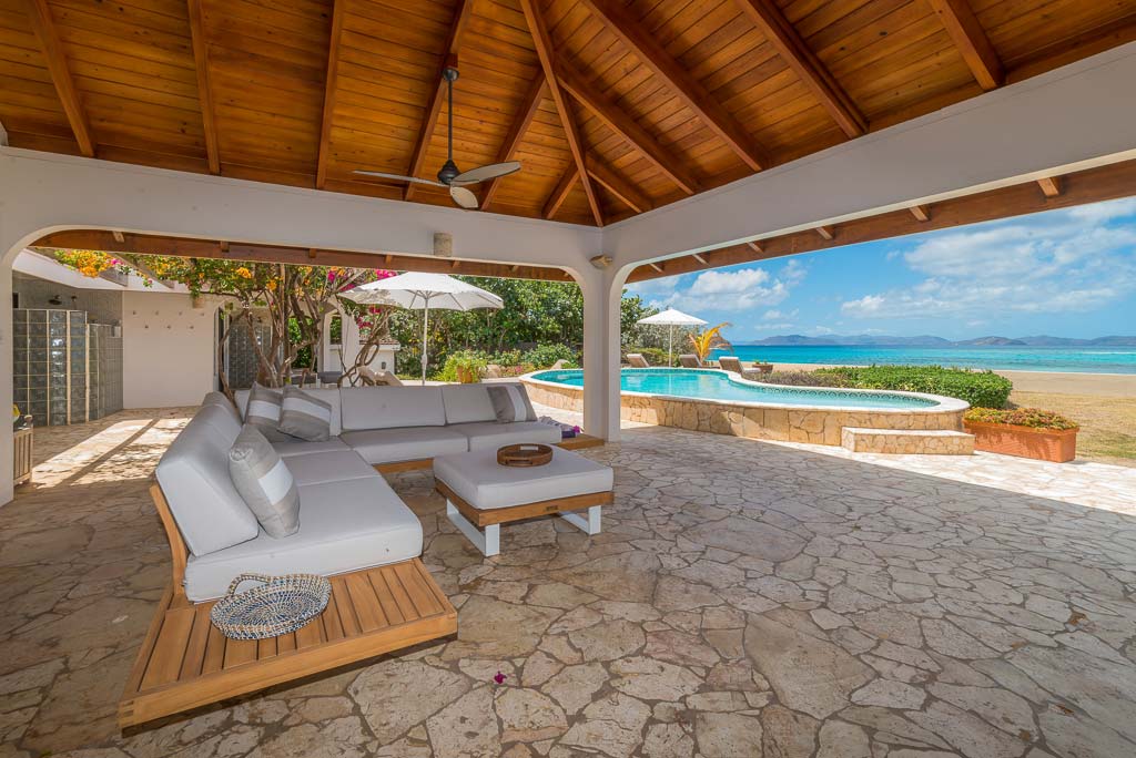 Covered stone patio at Sea Palms Villa adjacent to a swimming pool and the beach with beautiful Mango Bay in the background.