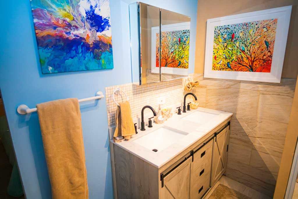 En-suite bathroom at 1 Paradise Lane Villa with colorful paintings on the walls, a tile backsplash and double sink.