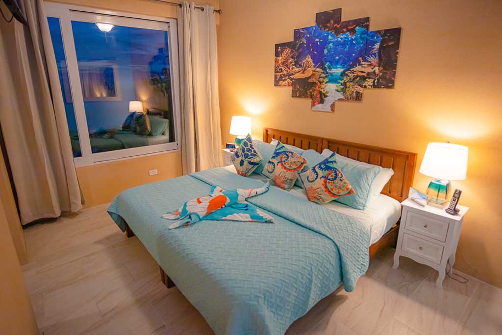 Guest room at 1 Paradise Lane Villa with a king bed, natural wood floors and a large window looking out on Nail Bay.