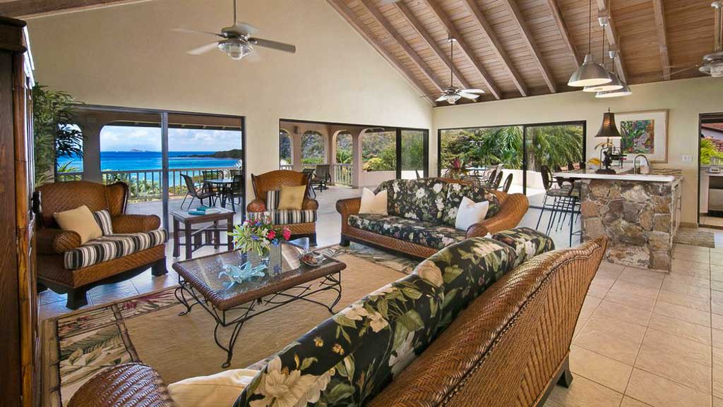 Adagio Villa's living area with comfortable wicker furniture and large windows looking out on a patio and Mahoe Bay.
