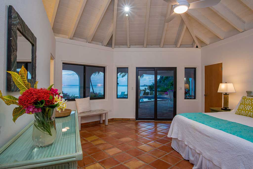 Beach Dream master bedroom suite with a king bed by a glass door leading to the pool deck with Mahoe Bay in the background.