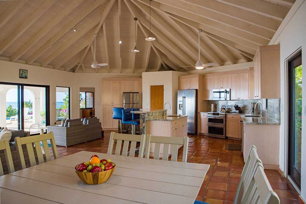 Dining area in the Beach Dreams Villa main room with an open kitchen and glass door to the patio in the background.