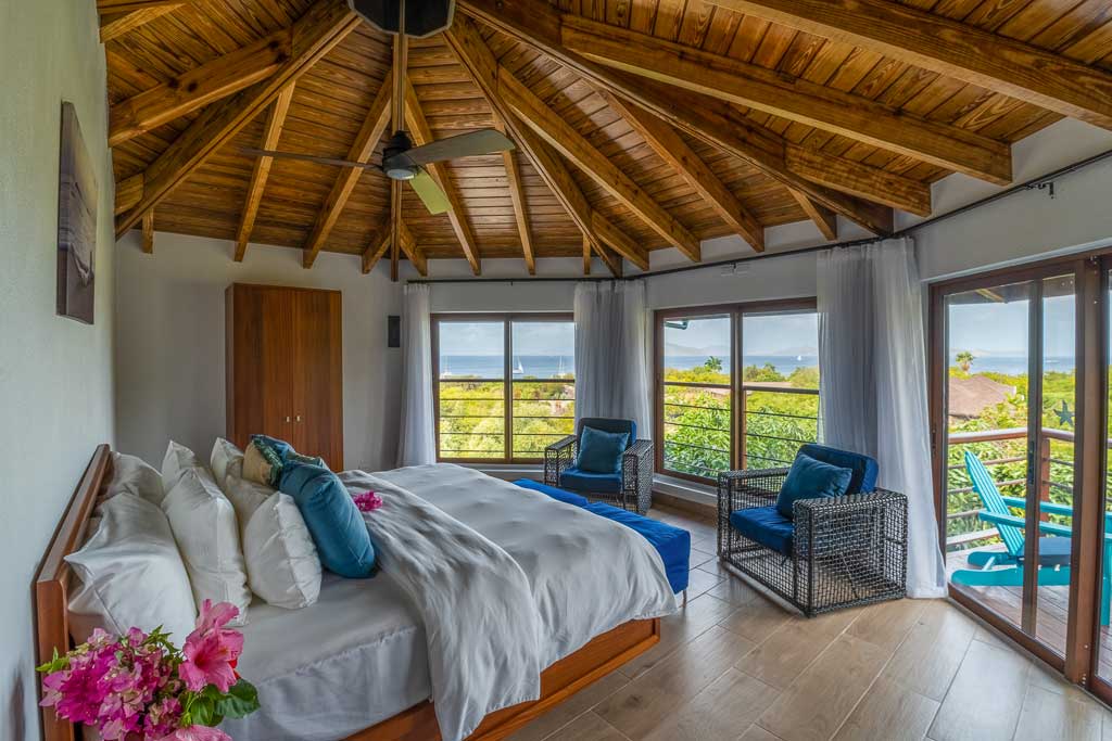Guest room at Eden Waters Villa with a king bed, large windows, a lofted, wood-beam ceiling and a door to a private balcony.