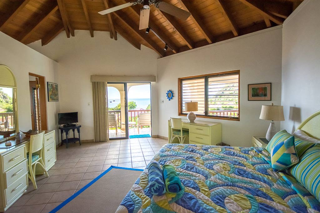 King bedroom at Loblolly Villa with tile floors, lofted wood ceiling and glass doors to a patio with the sea in the distance.