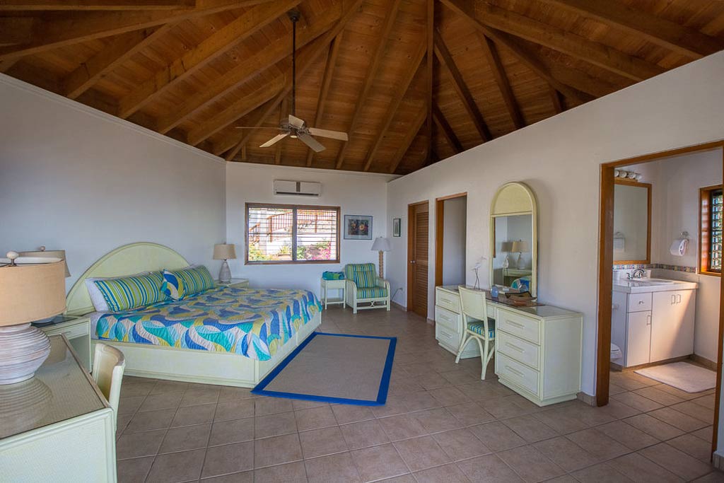 Spacious master bedroom at Loblolly Villa with a king bed, desk and chair, high ceiling and a door open to the en-suite bath.