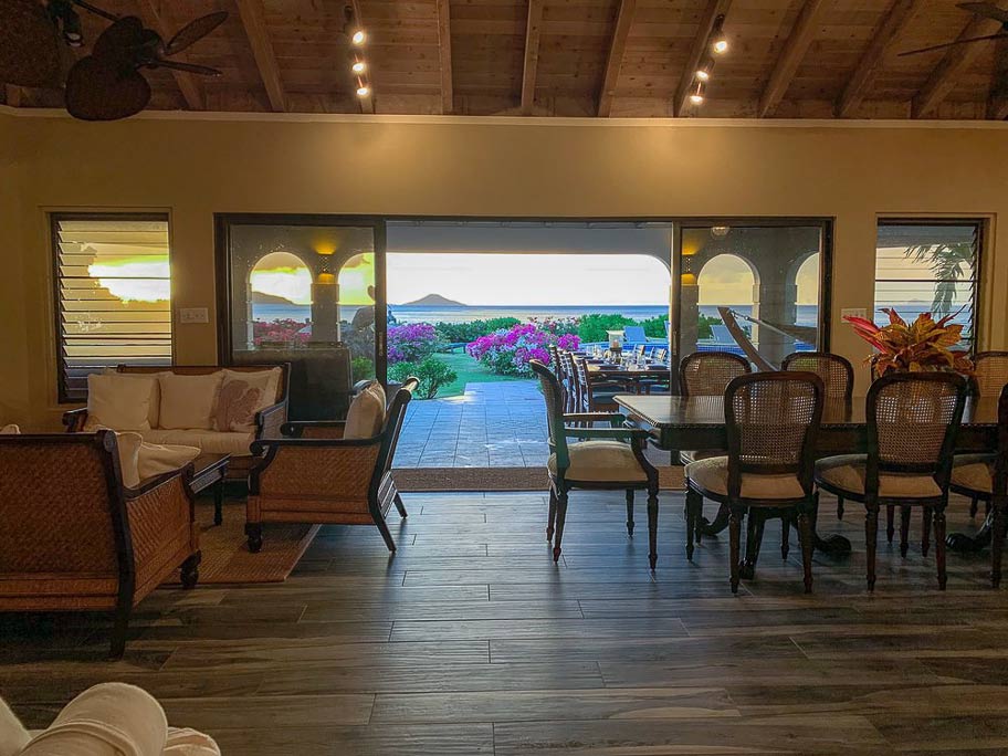 Dining and living areas in the main room at Sandcastle Villa with an open door to the patio, garden and bay in the background.