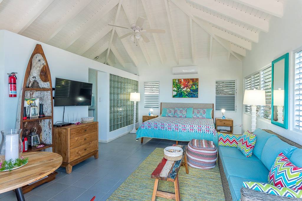 Sea Breeze Villa’s large bedroom suite with a king bed, colorful décor, flat-screen TV and lofted white wood-beam ceilings.