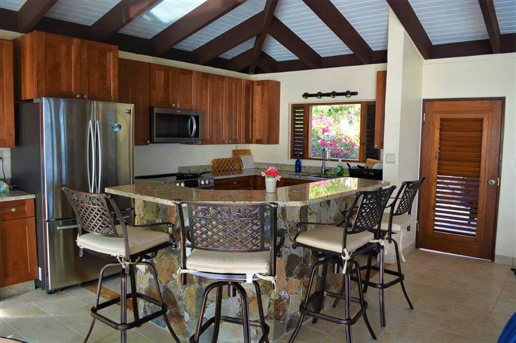 Kitchen at Serendipity Villa with stainless steel appliances and a stone island with a granite-top and high-back stool chairs.