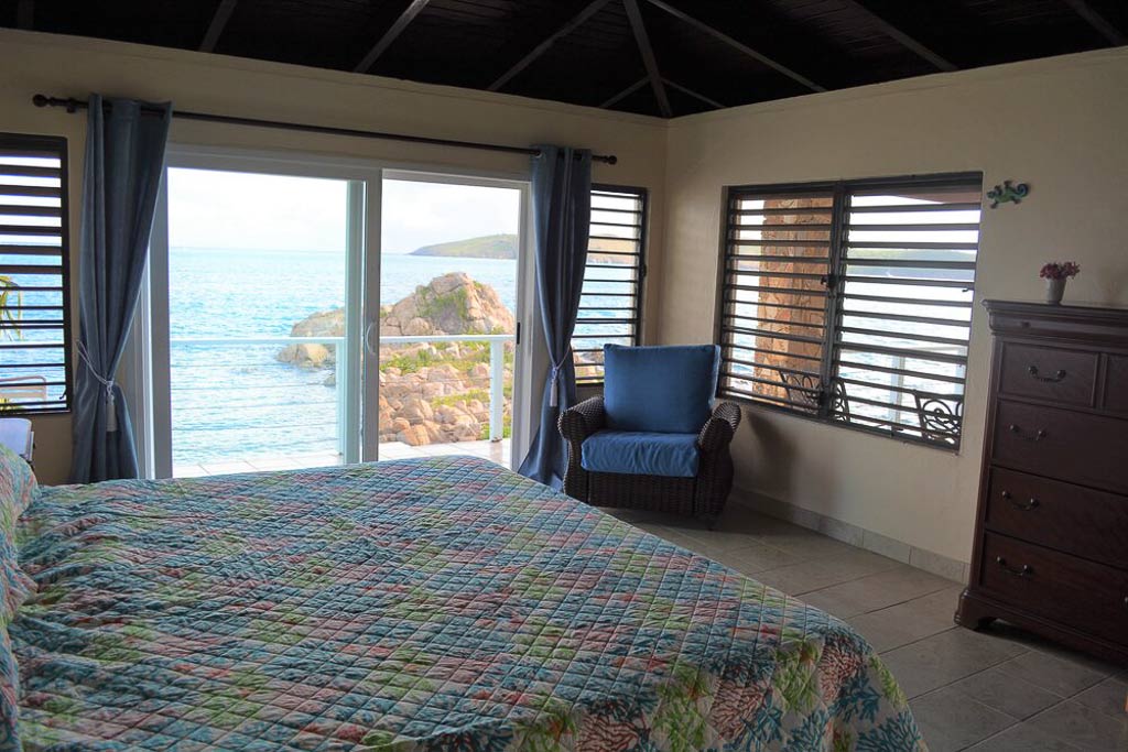 Serendipity guest bedroom with a sitting area and sliding glass doors to the patio with Leverick Bay in the background.