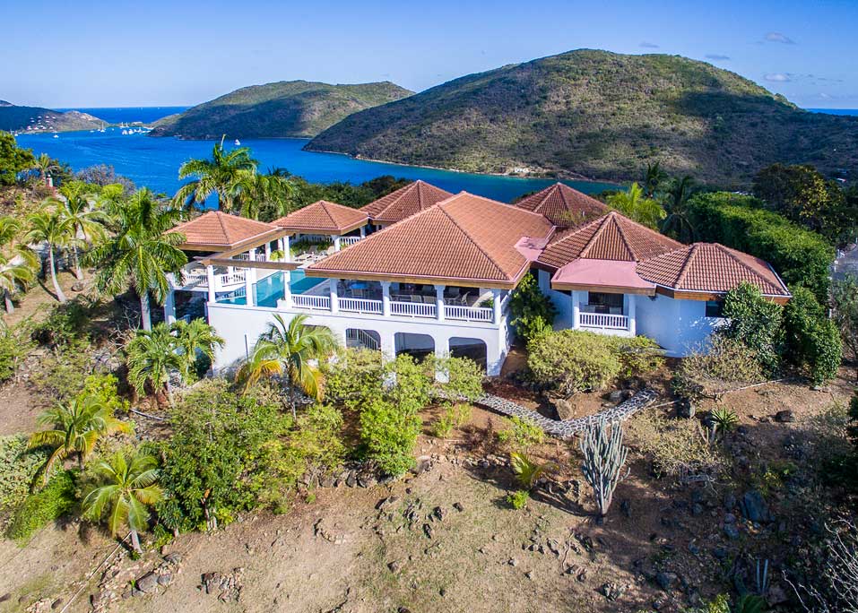 The sprawling white façade and red tile roofs of Villa Tamar on the tropical hillside with Leverick Bay in the background.