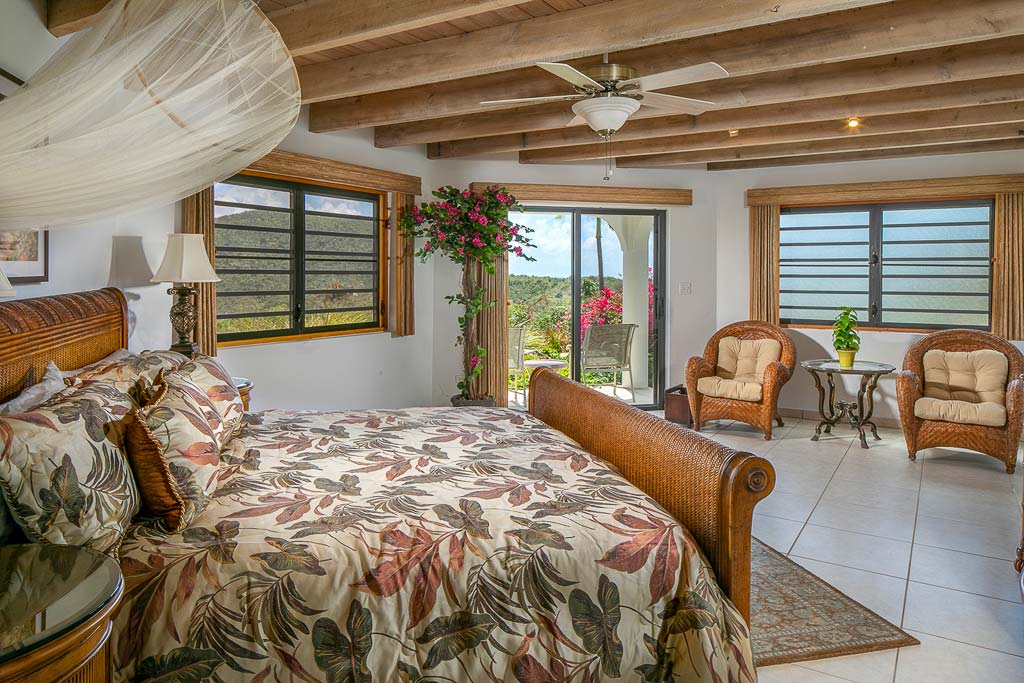 Master bedroom at Villa Tamar with a king bed and wood-beam ceilings with fan, sitting area and glass door to a private patio.