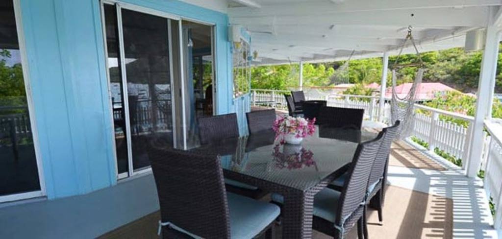 The dining area on the covered patio outside the main room at Vista Villa with chairs and a hammock in the background.