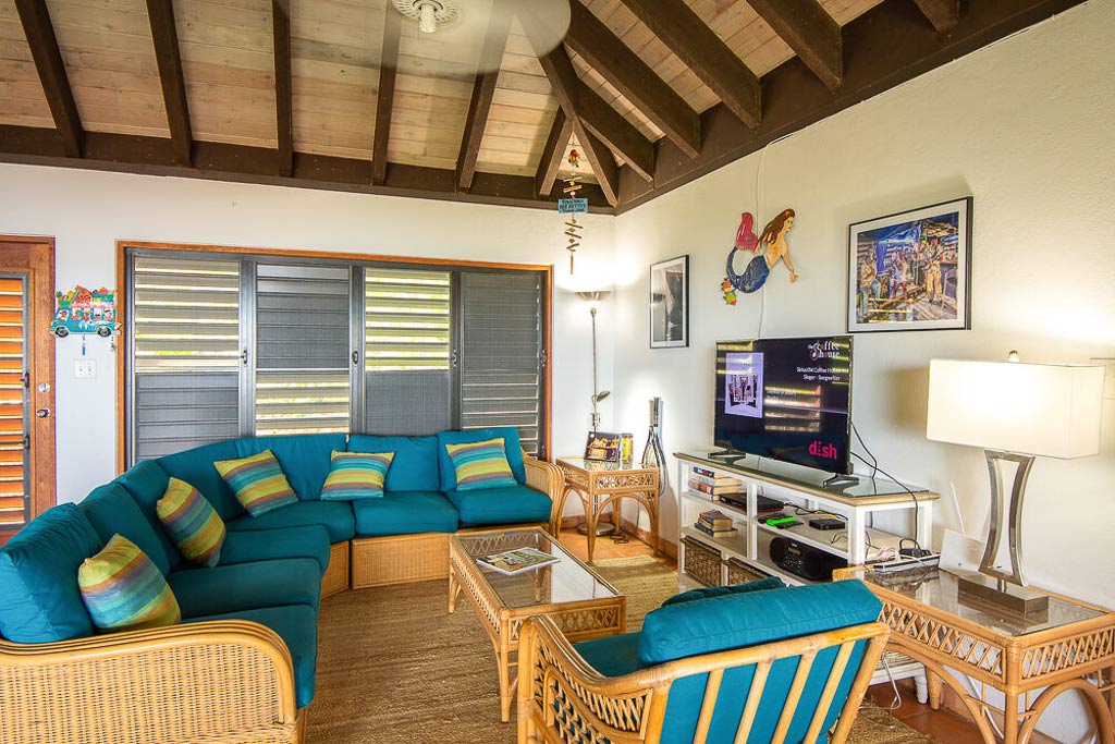Living and entertainment area in Villa Del Sole’s main room with wicker furniture with colorful cushions and a flat-screen TV.