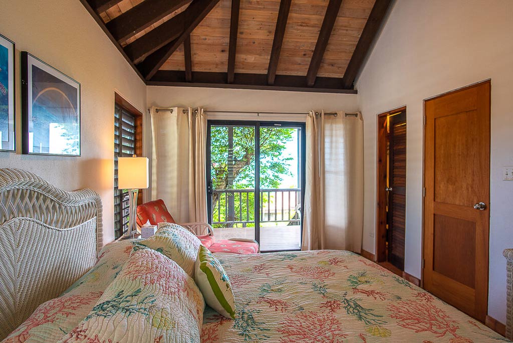 King bedroom at Villa Del Sole with natural hues and a wood-beam ceiling and a sliding glass door to a private patio.