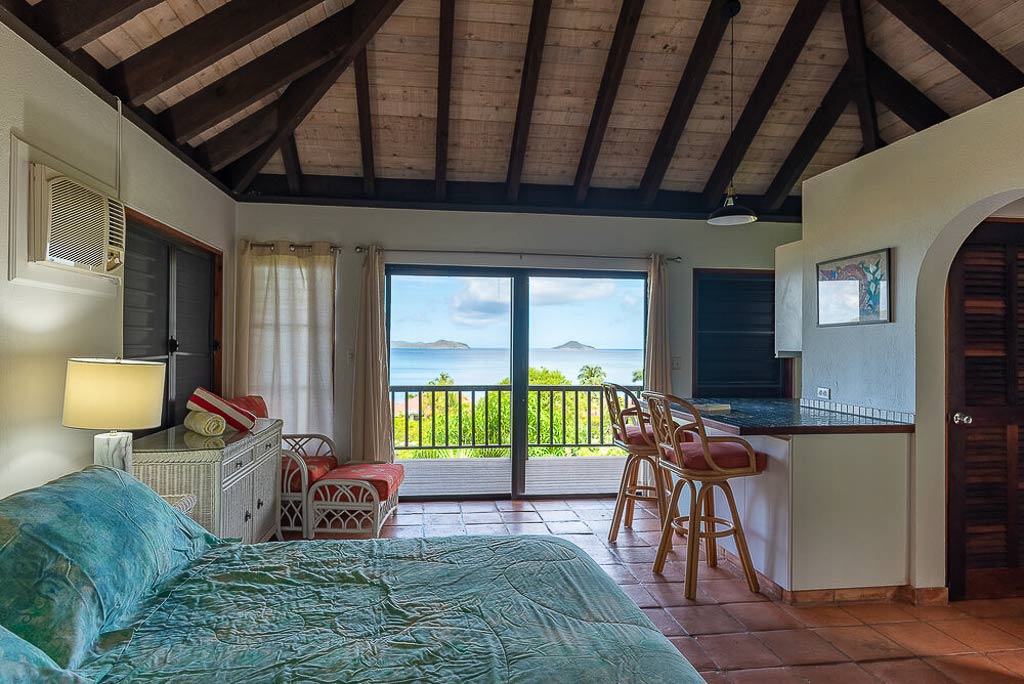 Villa Del Sole guest room with a king bed, tile floors, vaulted ceilings and a glass door to a patio looking out on Mahoe Bay.