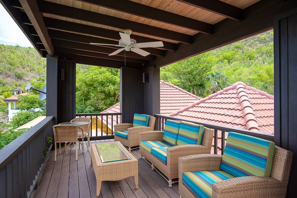 Viewing deck with colorful patio furniture and a wood-beam ceiling with a fan and the hills of Mahoe Bay in the background.