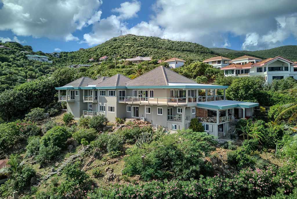 Coconut Grove luxury villa sitting on the lush green hillside with a natural stone path leading down toward Leverick Bay.