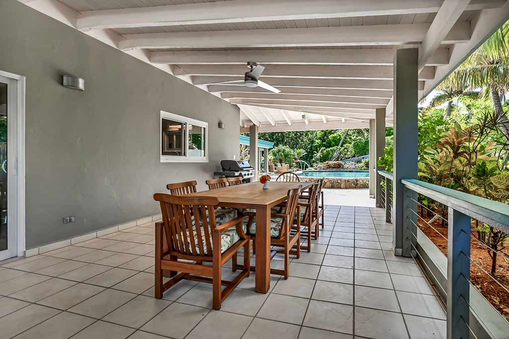 Covered outdoor patio at Coconut Grove with a wooden dining table with eight seats and a grill and pool in the background.
