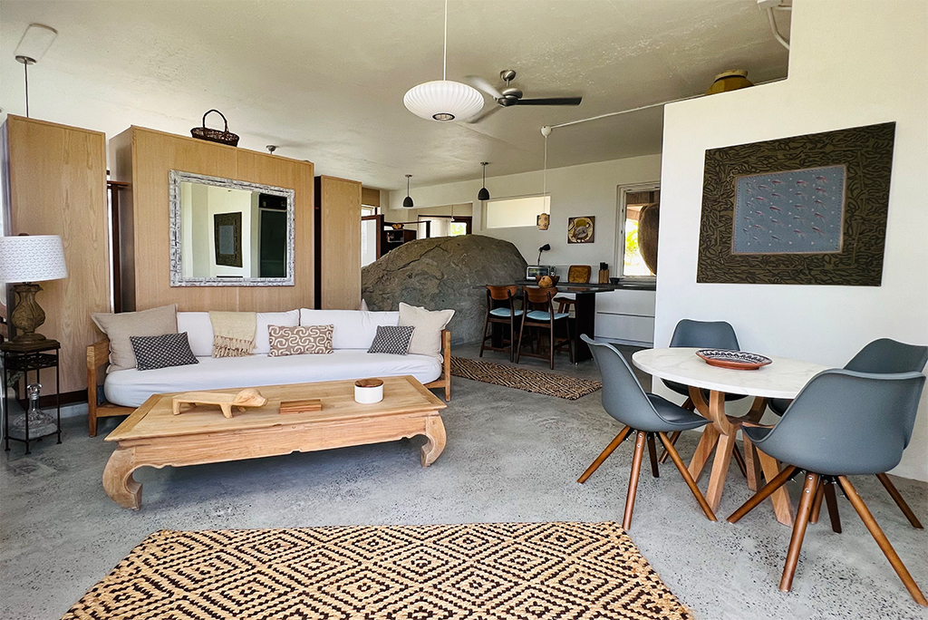 Beachrock Villa interior with separate living and dining areas and a desk and a large local boulder in the background.