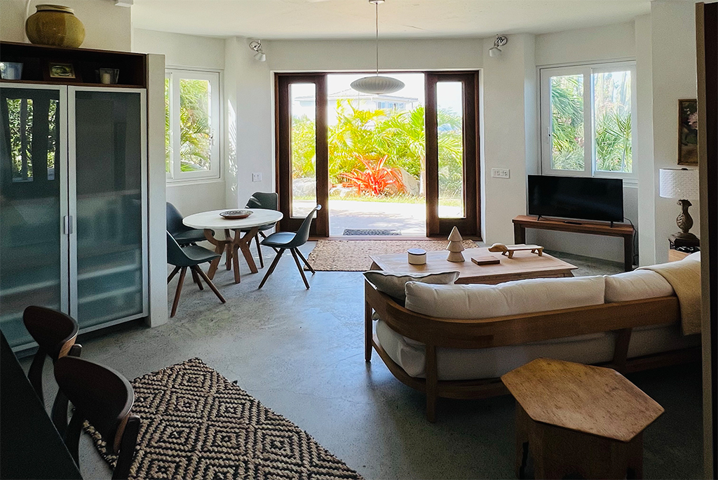 Inside Beachrock Villa’s main room with a couch area, TV and breakfast nook looking out to the open front door and garden.