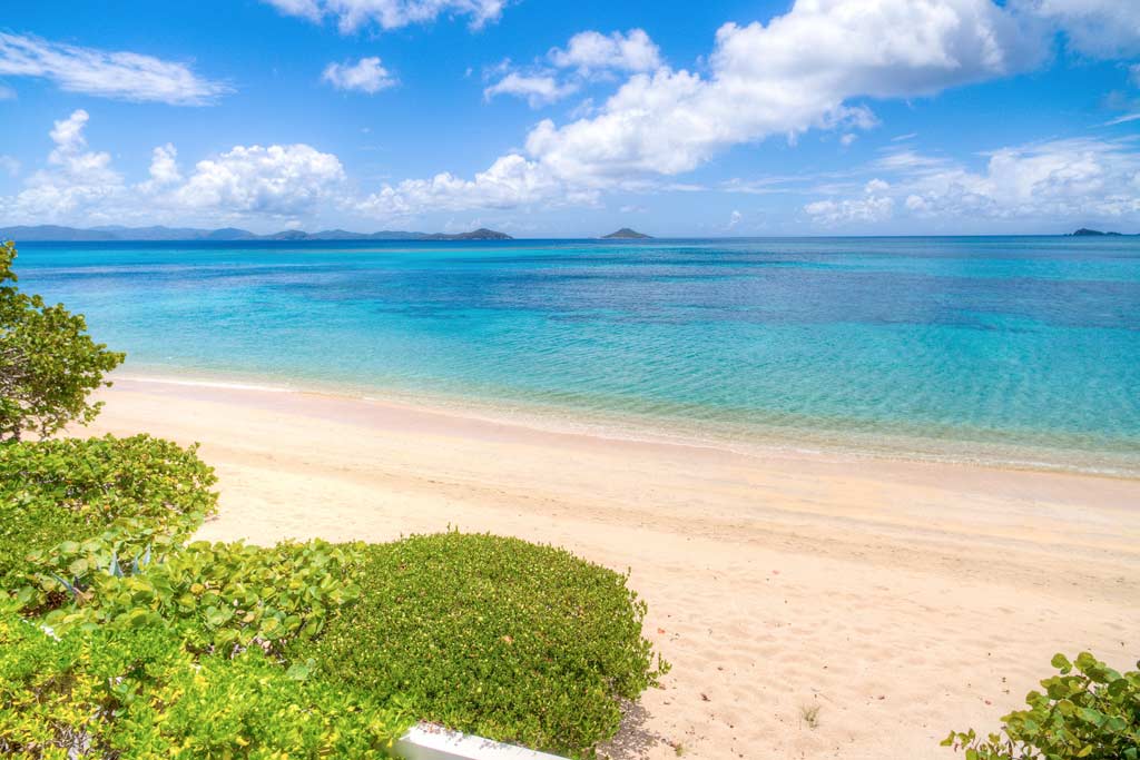 Beachfront at Sea Fans Villa on Mahoe Bay with a white sand beach and crystal blue waters on a bright sunny day.
