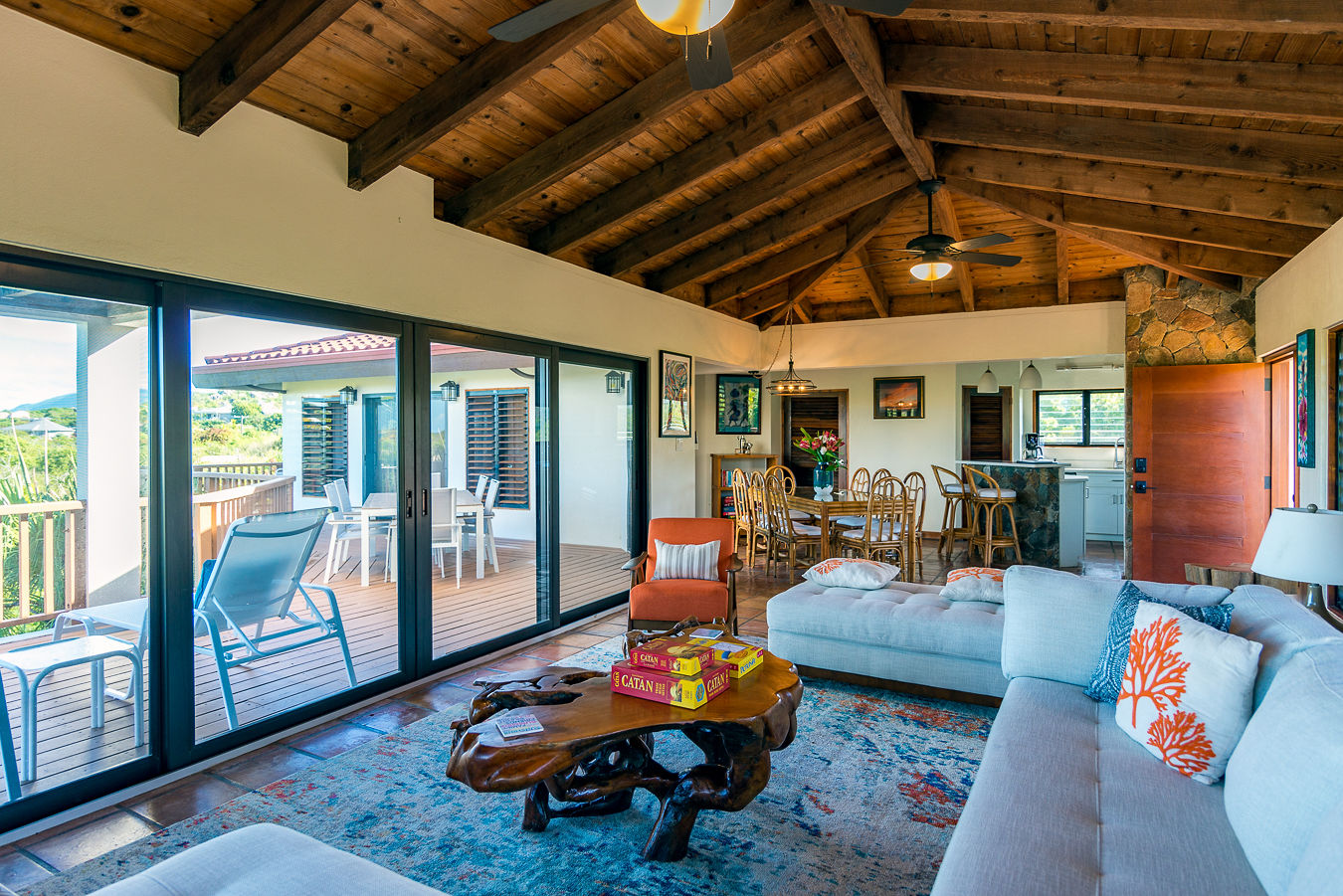 Living area in Amani Villa’s main room with comfortable couches, glass doors to a deck and a dining area in the background.