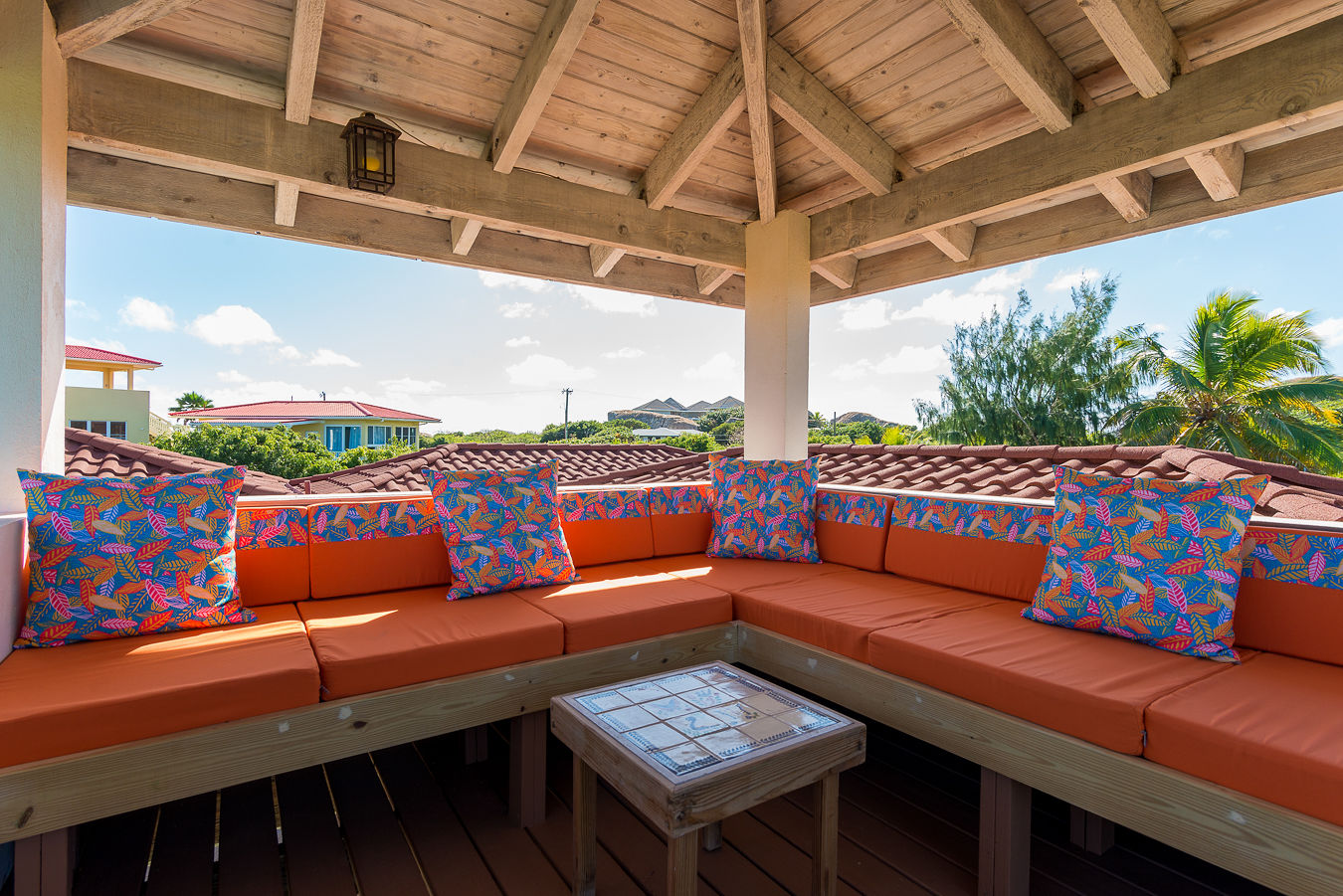 Covered outdoor viewing platform with a wrap-around orange cushioned couch and colorful pillows looking out on a sunny sky.