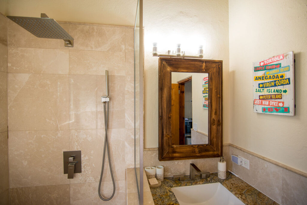 Amani Villa bathroom with a granite-top vanity, a shower stall and a painting listing the BVI islands with direction arrows.