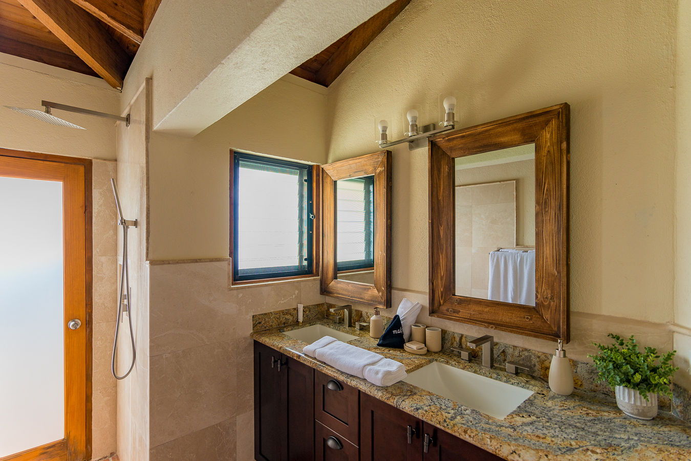 Amani Villa’s master bathroom with a granite-counter double vanity, tile and natural stone walls and a shower.